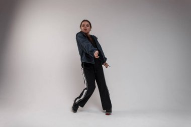 Çekici genç kadın dansçı modern dans bir odada beyaz bir arka plan üzerinde dans spor ayakkabı siyah eşofmanlı siyah bir t-shirt, kot mavi gömlekli. Sevimli kız