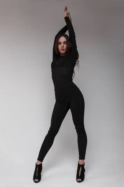 Cute athletic young beautiful woman dancer in stylish black leggings in a  black pullover in black sports sneakers posing in a studio near a white  wall. Attractive girl Stock Photo