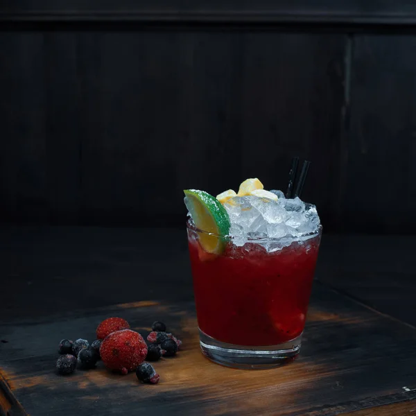 酒吧的木桌上矗立着一杯红色的甜冷酒鸡尾酒和新鲜的浆果和石灰片 鸡尾酒冷 原汁原味的饮料 — 图库照片