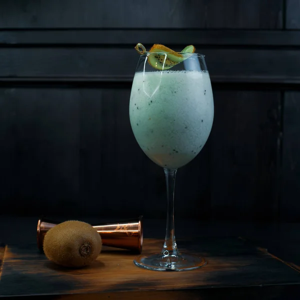 牛奶酒精鸡尾酒与松果和椰子糖浆装饰与一片猕猴桃站在一个优雅的玻璃木制的老式桌子旁边的金属玻璃和猕猴桃 美味的甜饮料 — 图库照片