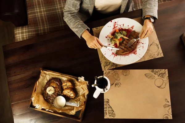 A solid lady sits at a table in a luxurious restaurant and eats a steak \