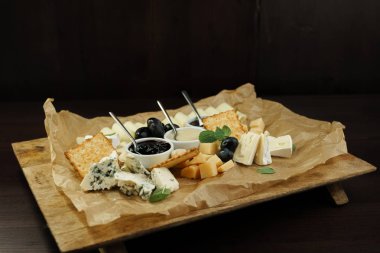 Set: Parmesan peyniri, Gouda peyniri, beyaz peynir, mavi peynir tatlı bal ve İsveç kirazı reçel, güzel kokulu fesleğen yaprakları ve zeytin bir restoranda masanın üzerine ahşap bir gemide süslenmiş ile. 
