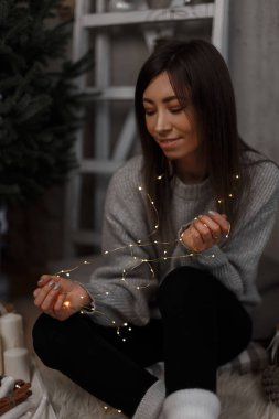 Yeni yıl oda katta oturan muhteşem ışıkları hayal ile genç güzel kadın. Gülümseyen güzel kız.