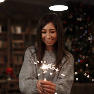 Örme kazak genç mutlu kadın inanılmaz bir maytap vintage bir odada onun elinde tutar. Mutlu Noeller ve mutlu yeni yıl. Gülümseyen kız.