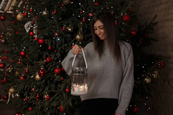 Mutlu genç kadın şık örme kazak şamdanla elleri şenlikli bir oda içinde yaşayan Noel ağaç arka plan karşı duruyor. Pozitif kız.