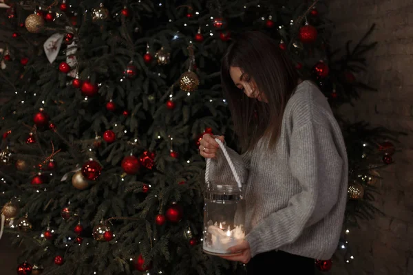 Genç mutlu kadın kazak örme bir vintage içinde oyuncaklar ile dekore edilmiş bir Noel ağacı arka plan üzerinde yanan bir mum ile bir güzel cam şamdan elinde tutuyor. Neşeli kız.