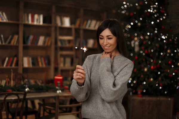 Örme sıcak kazaklı genç kadın bir maytap onun el gülümsüyor tutar ve arka plan şenlikli bir odada vintage bir kitaplık yakın görünüyor. Neşeli kız.