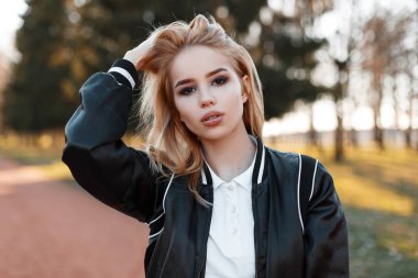Seksi genç güzel sarışın bir kadın moda hafif siyah bir ceket ağaçlar arka plan üzerinde şık beyaz gömlekli ve günbatımı Park portresi. Şaşırtıcı Amerikan Kız.