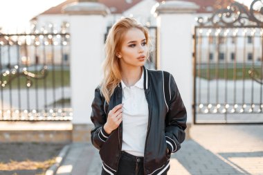 Çok çekici genç kadın sarışın siyah bahar şık ceket siyah kot pantolon beyaz gömlek beyaz bina karşı vintage gate yakınındaki teşkil etmektedir. Amerikan şık kız. Modern moda