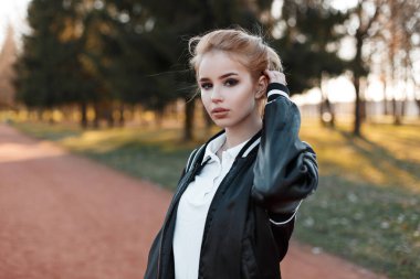 Genç güzel sarışın kadın moda hafif siyah ceket yeşil ağaçlar arka plan üzerinde şık bir beyaz gömlek ve günbatımı Park kahverengi gözlü. Sevimli kız açık içinde yürür. 