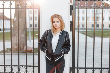 Çok güzel sarışın kadın siyah bahar şık ceket siyah kot pantolon beyaz gömlek vintage Iron gate günbatımında duruyor. Moda kız. Modern Amerikan moda