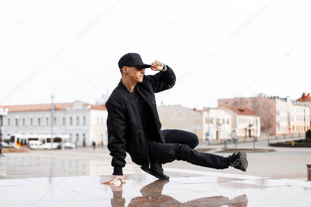 Stylish young male dancer in fashionable black clothes dancing blake dance on a street in the city on an autumn afternoon. Lifestyle.