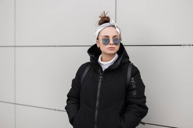Avrupa şık genç kadın hippi kenti yakınlarındaki beyaz bir duvar poz şık bandana ile şık bir saç modeli ile şık siyah paltolu. Amerikan tarzı kadın giyim.