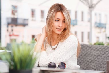 Masada sokak bir kafede güzel çekici genç kadın sarışın bir moda örgü süveter tatlı bir gülümseme ile oturuyor. Şaşırtıcı kız sıcak yaz günü hoşlanır.