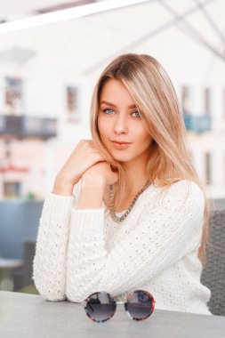 Mavi gözlü kazak örme bir vintage çekici güzel genç kadın oturma ve sıcak güneşli bir günde açık bir kafede kamera bakıyor. Avrupa modern kız dinlenme.