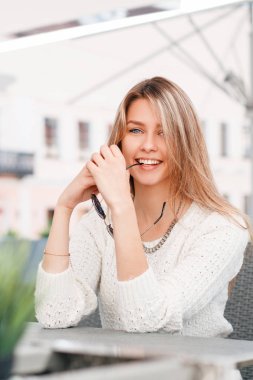 Komik şirin genç sarışın kadın vintage örme beyaz kazaklı sokak bir kafede bir masada oturuyor. Tatil güzel kız.