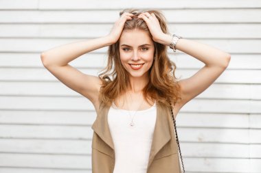 Bir zarif yaz bej neşeli genç kadın yelek bir şık tişört ahşap vintage beyaz duvara yakın poz içinde. Neşeli kız güzel bir gülümseme ile. Olumlu ruh hali