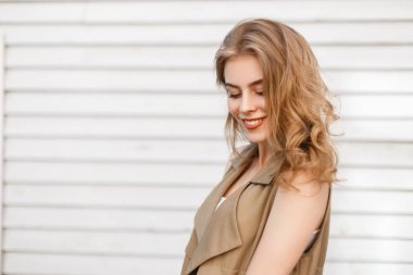 Sevimli çekici genç kadın şık yazlık giysiler içinde güzel bir gülümsemeyle bir beyaz tahta duvar açık havada duruyor. Sevimli mutlu pozitif moda kız.