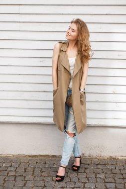 Neşeli mutlu genç kadın bir yaz aylarında şık tişört şık yırtık kot pantolon siyah yüksek topuk ayakkabı, siyah bir çanta bir ahşap beyaz duvar poz ile yelek. Bir yolda sevimli kız