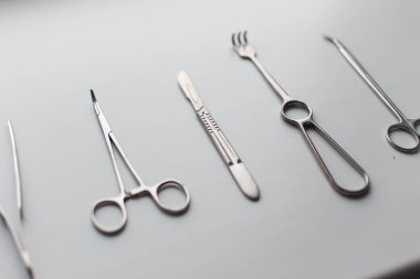 Tıbbi aletleri (neşter bıçak, makas, pens, kelepçeler, forseps) odada beyaz bir arka plan üzerinde metal kümesi. Modern profesyonel krom araçları.