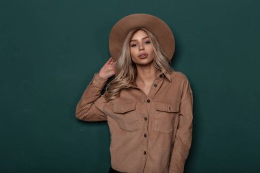 Seksi arsız genç sarışın kadın kıvırcık saçlı güzel makyaj yakınındaki bir yeşil duvar arka plan bej trendy gömlekli vintage zarif şapkalı bir portresi. Şehvetli sihir kız.