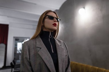 Güzel şık genç hipster kadın siyah trendy güneş gözlüğü gri şık kareli ceket kırmızı dudaklar ile deldi burunlu bir kafede poz şaşırtıcı. Modern kız. Retro tarzı kadın moda.