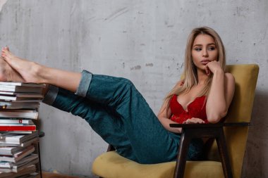 Lüks kırmızı dantel iç çamaşırı şık Jeans sarı saçları çekici seksi genç kadın dergileri gri duvarının yakınında Studio'da yığını yakın vintage bir sandalyede oturur. Şık güzel kız.