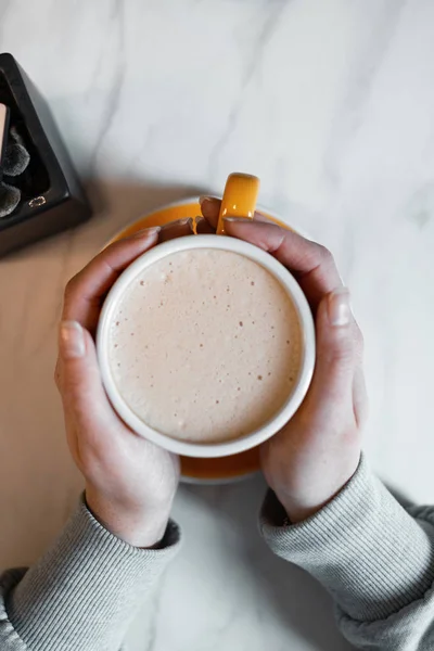 Vrouwelijke handen houdt een kop met heerlijke koffie met slagroom op de achtergrond van een vintage tafel in een café. Ochtend koffiepauze. Close-up. Van bovenaf bekijken. — Stockfoto