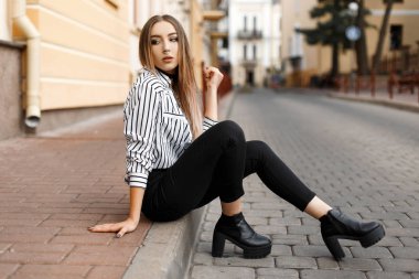 Modern çekici şık genç kadın şık bir bluz siyah kot pantolon deri ayakkabı içinde bir vintage building yakınındaki sokakta oturan dinleniyor. Çok Avrupa kız yaz gün açık havada zevk