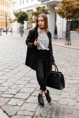 Modaya uygun kot pantolon moda deri ayakkabı bir çanta ile şık bir bluz şık bir ceket deldi burnuna olan kadın vintage binalar yakınındaki şehirde cadde boyunca yürür. Sevimli kız.