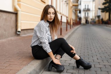 Şık bir bluz siyah kot pantolon deri ayakkabı modern şık genç kadın vintage bir binanın yakınında sokakta oturan dinleniyor. Çok Avrupa kız yaz gün açık havada zevk