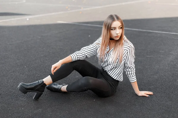 Hermosa joven en una elegante blusa a rayas en blanco y negro en jeans en zapatos de cuero con una nariz perforada descansando al aire libre en un día de verano. Elegante chica adolescente disfruta de fin de semana —  Fotos de Stock