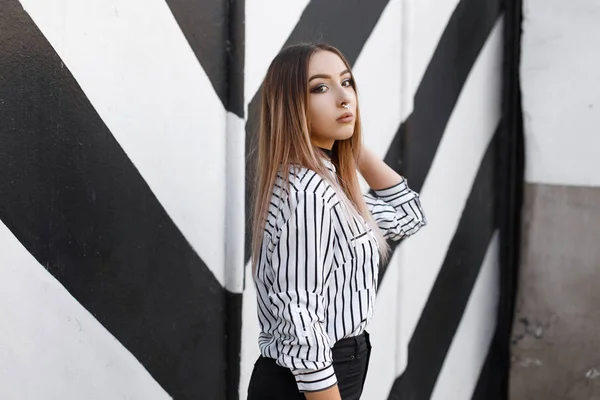 Mujer joven bastante de moda en una camisa de rayas vintage con la nariz perforada en un collar de terciopelo en jeans negros elegantes posando cerca de una pared en blanco y negro en rayas. Hermosa chica sexy modelo . —  Fotos de Stock