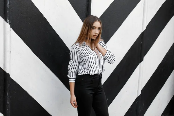 Fashionable young woman in trendy black and white striped shirt with nose piercing in black jeans in a velvet necklace posing near a vintage wall. Cute teenager girl model on a walk. — Stock Photo, Image
