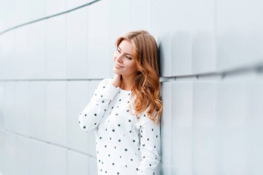 Şık kıyafetler sevimli Avrupa olumlu genç kadın ayakta ve beyaz modern duvar kapalı yakın gülümseyen. Tatil şık pozitif kız modeli.