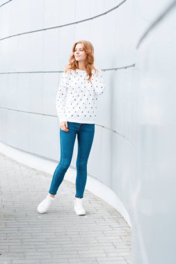 Duvar yakın moda beyaz spor ayakkabıları şık mavi kot Vintage bir kazak Avrupa ince şık genç kadın. Pozitif neşeli model kız şehir etrafında bir yürüyüş zevk.