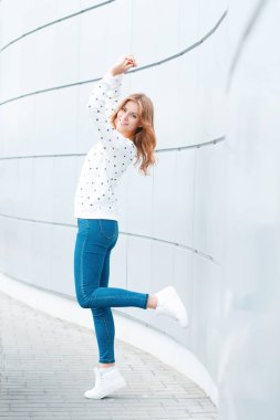 Şık kıyafetler neşeli güzel olumlu genç kadın modern duvarın yakınında sıcak bir bahar gününde kapalı eğlenin. Şık Avrupa kız moda kot mutlu. Bahar tarzı gençlik giyim