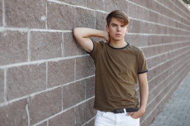 Sokakta bir taş Vintage duvar yakın poz trendy beyaz pantolon yeşil şık t-shirt şık saç modeli ile genç yakışıklı Modern adam. Amerikan adam açık havada dinleniyor.