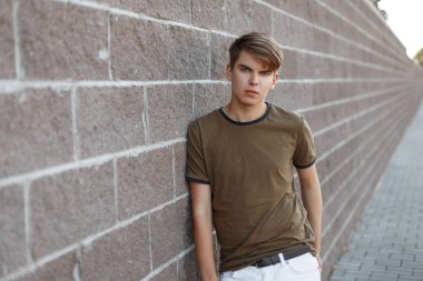 Yaz trendy giysiler şık saç modeli ile çekici şık genç adam şehirde bir Vintage taş duvar yakınında duruyor. Sıcak bir yaz gününde bir yürüyüşe Amerikan adam.