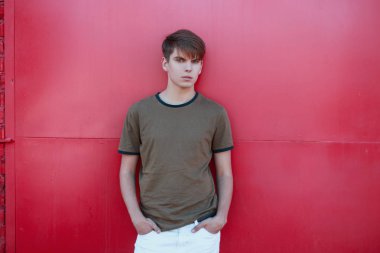 Beyaz pantolon yeşil şık t-shirt şık bir saç modeli ile yakışıklı modern genç adam parlak pembe Vintage duvar yakın pozlar. Çekici adam açık havada rahatlatıcı. 