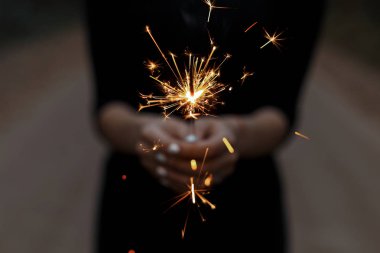 Siyah t-shirt açık havada bir genç kadının elinde havai fişekleri yanan turuncu. Kız şenlikli bir Bengal ateş etmeyin. Doğum günün kutlu olsun. Yakın çekim.