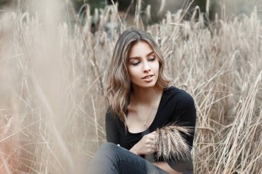 Trendy kot şık bir siyah t-shirt sevimli güzel mutlu genç kadın kuru sonbahar çim açık havada oturan istirahat. Neşeli kız köyde doğa sahiptir. Büyük hafta sonu.