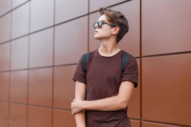 Vintage kahverengi bina yakın bir siyah spor sırt çantası şık bir t-shirt siyah şık güneş gözlüğü genç yakışıklı modern hipster adam. Şehirde çekici Amerikan adam seyahat.