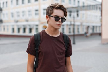 Bir spor sırt çantası ile moda kahverengi tişört şık güneş gözlüğü çekici şık genç hipster adam şehir boyunca yürür. Tatildeki Modern adam. Erkek moda.