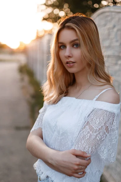 Junge hübsche attraktive Frau mit blauen Augen und natürlichem Make-up in einem eleganten Spitzenshirt, das an einem sonnigen Tag im Freien neben einem Vintage-Zaun posiert. schöne süße Mädchen genießt die Natur. — Stockfoto