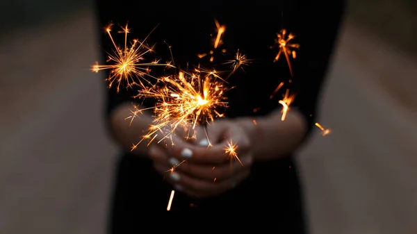 Increíbles bengalas festivas en manos de una joven. Chica celebra feliz cumpleaños. Chispas de color naranja brillante con un primer plano . — Foto de Stock