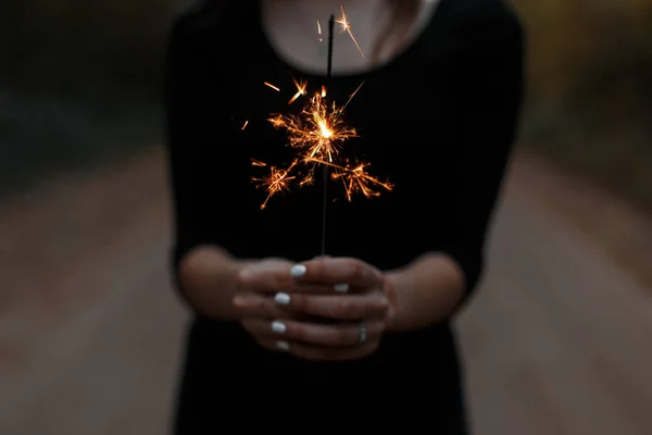 Mujer joven sostiene una brillante chispa festiva naranja en sus manos. La chica celebra su cumpleaños. Primeros planos de manos femeninas . —  Fotos de Stock