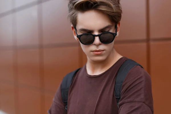 Guapo joven adolescente en gafas de sol de moda con un peinado en una camiseta de moda de verano en la calle. Retrato al aire libre del niño — Foto de Stock