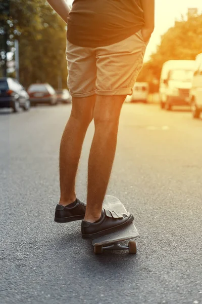 Jeune homme fait du skateboard autour de la ville. Beau temps avec un coucher de soleil. L'Américain moderne avance. Jambes d'hommes en baskets à la mode sur une planche à roulettes . — Photo