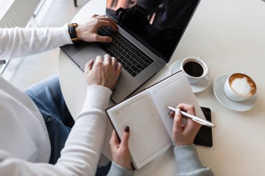 Kadın ve erkek yöneticiler modern bir ofisteki bir iş toplantısında beyaz masada oturup çalışma saatlerini tartışırlar. Meslektaşlar uzaktan çalışır. Masaüstünün üst görünümü.